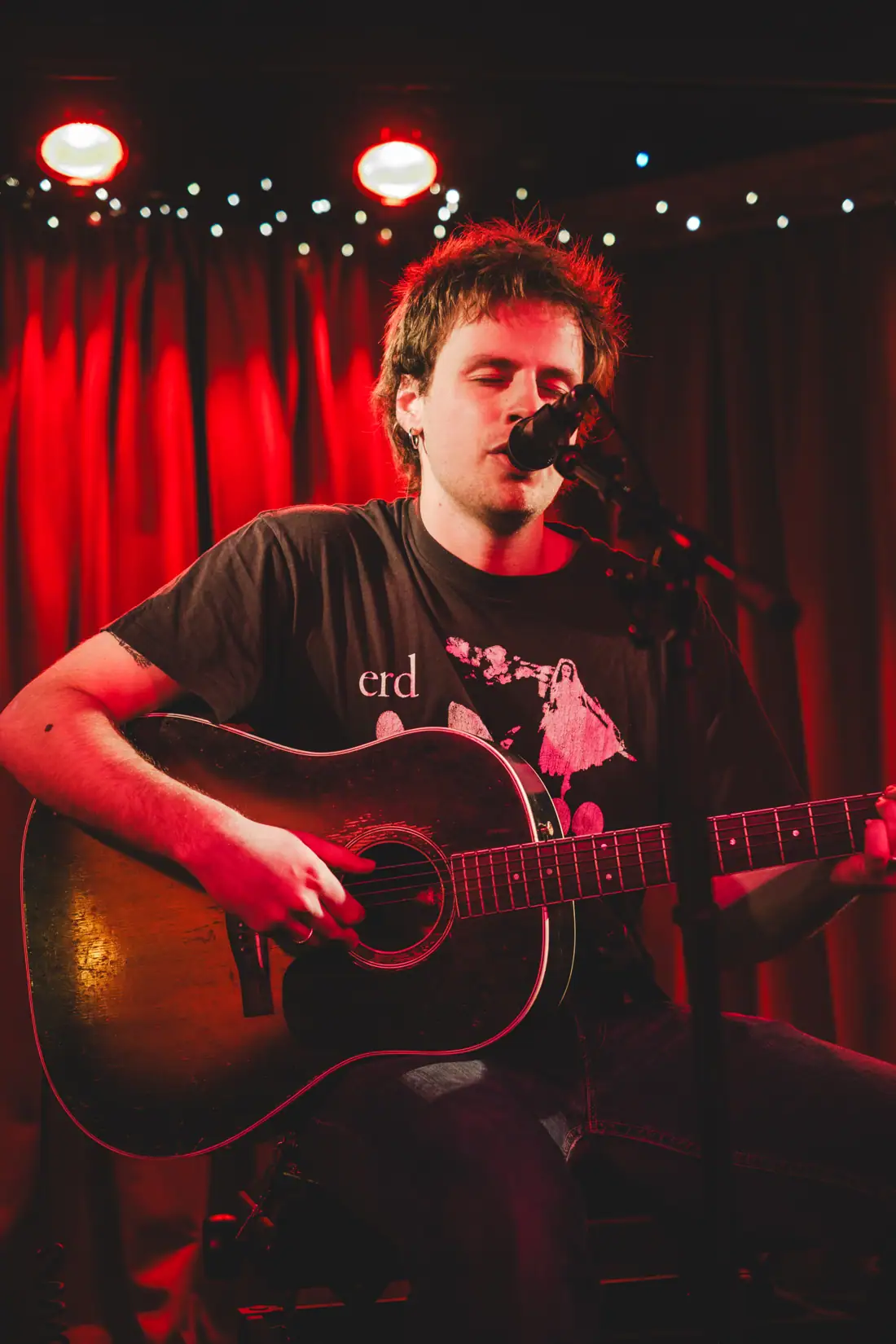Sam De Nef zingend met gitaar voor het neonbord