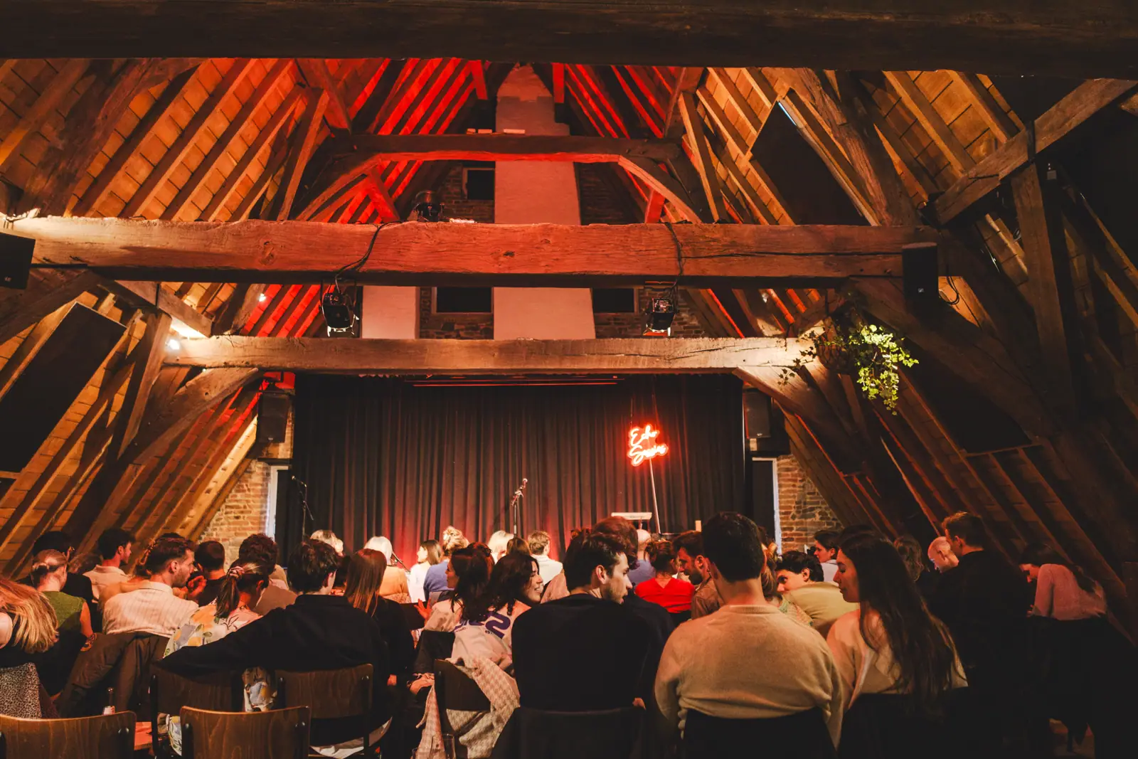 Zaal met houten spanten en publiek op stoelen, editie 2