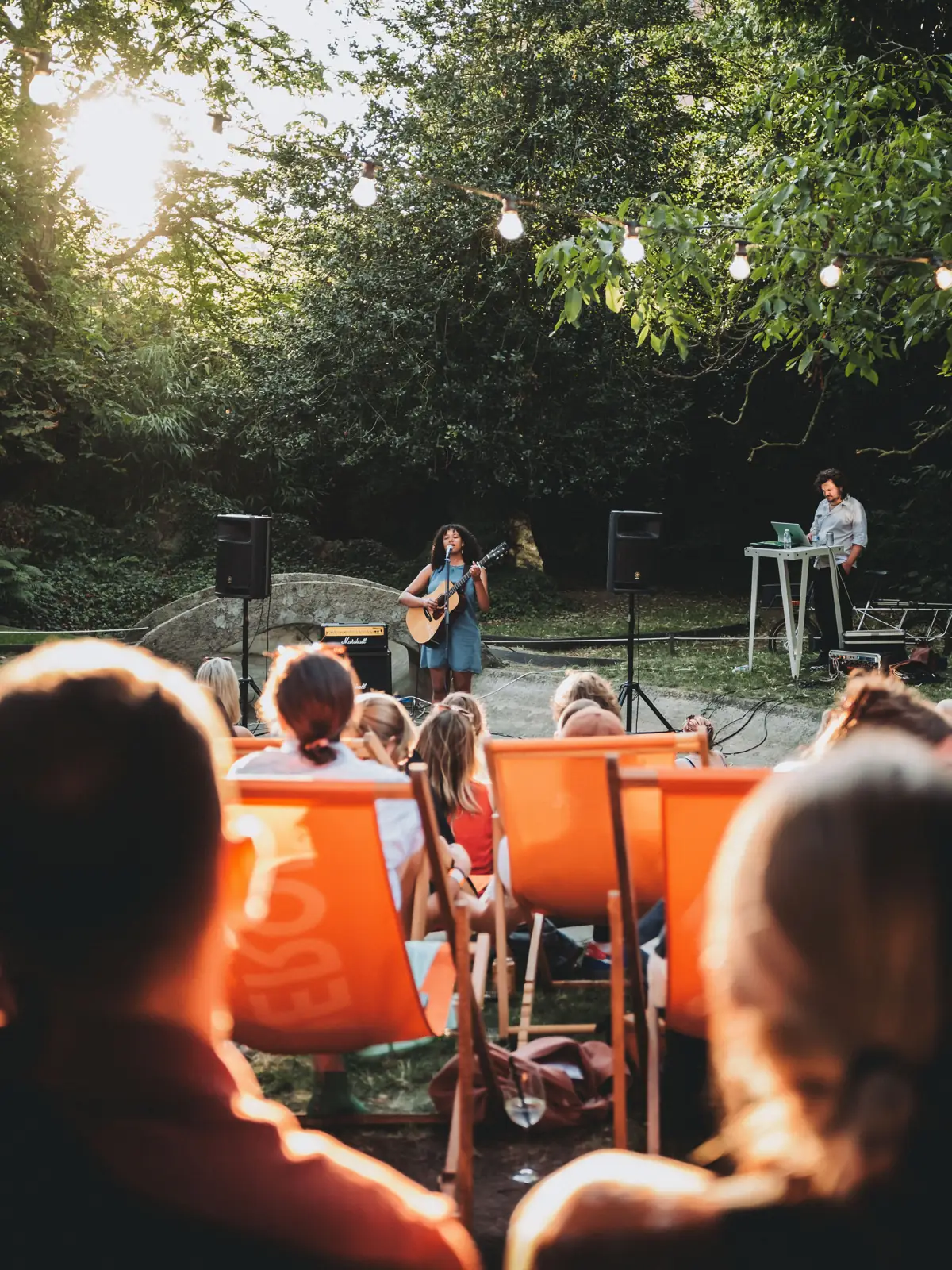 Publiek in ligstoelen kijkt naar een gitarist in tegenlicht, Sunset Concert