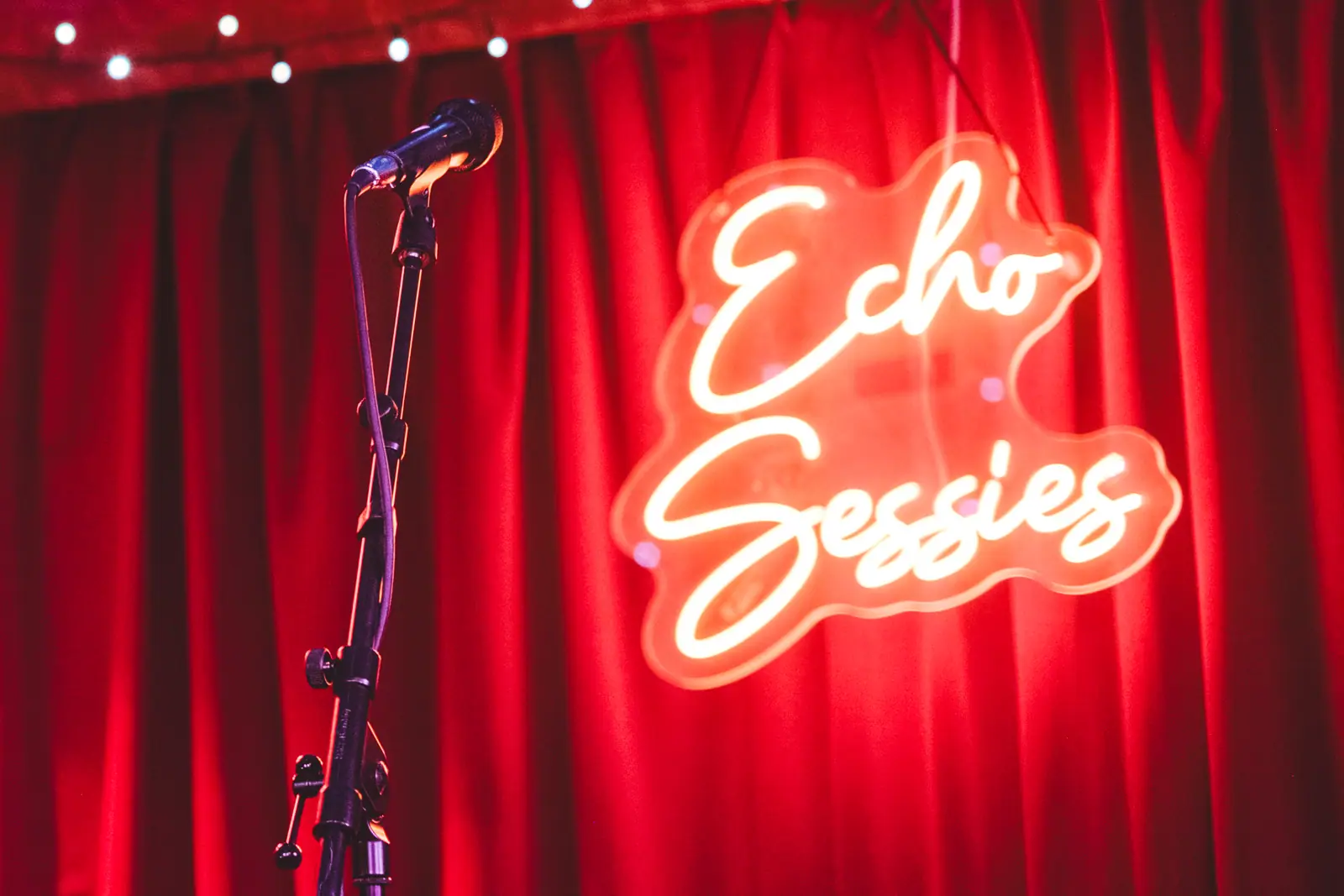 Het rode neonbord van Echo Sessies in cursief schrift voor een rood fluwelen gordijn